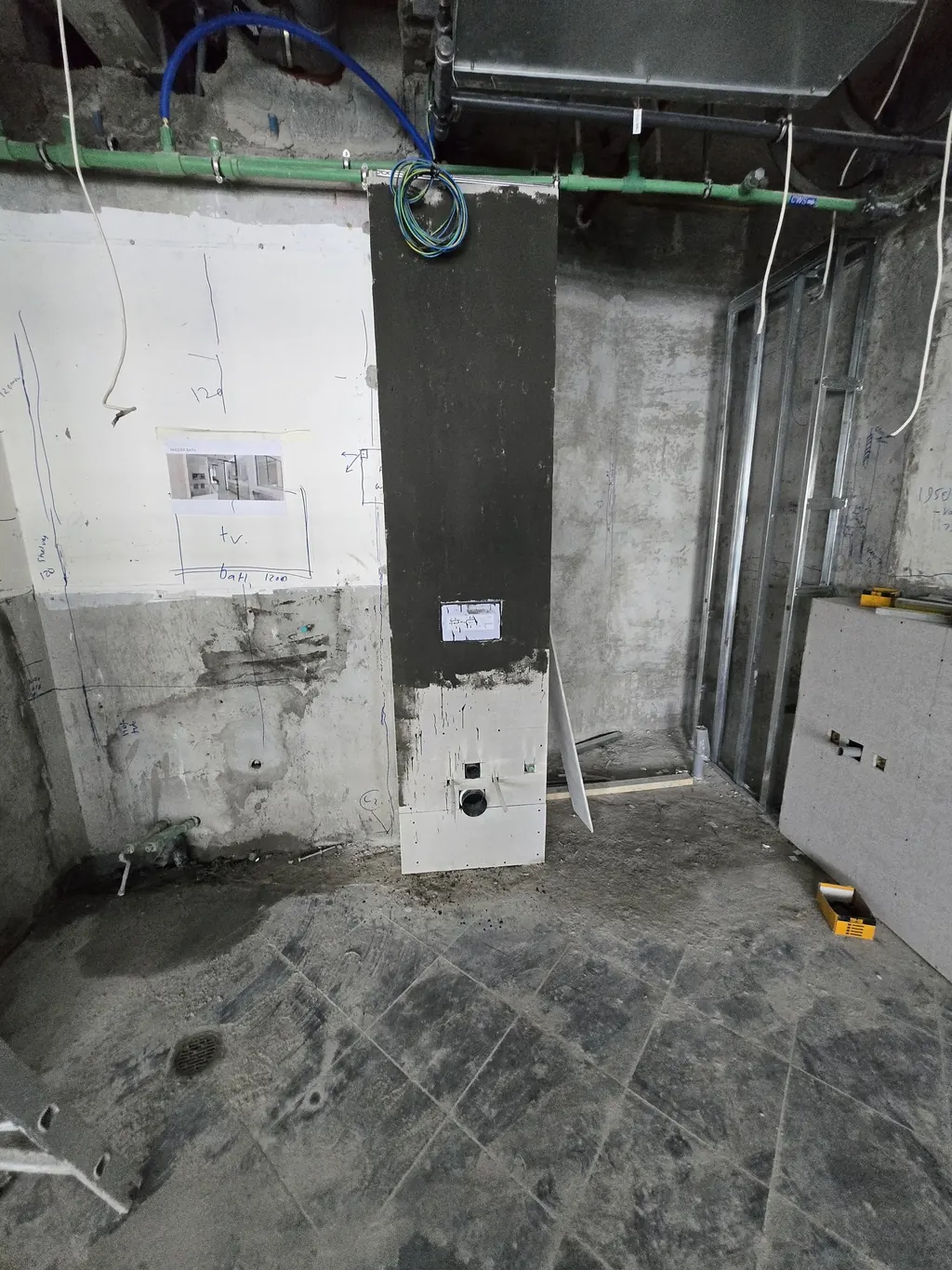 The master bathroom stripped back: the old floor still down, the WC column waterproofed, the bath and TV wall marked out in pencil