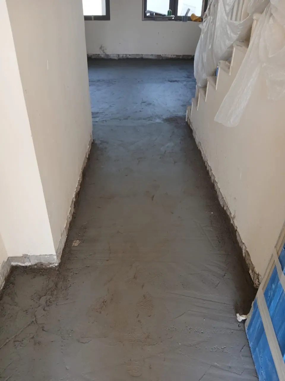 The hall beside the staircase during the works: new screed floor, the stair wrapped in protection, the window at the end