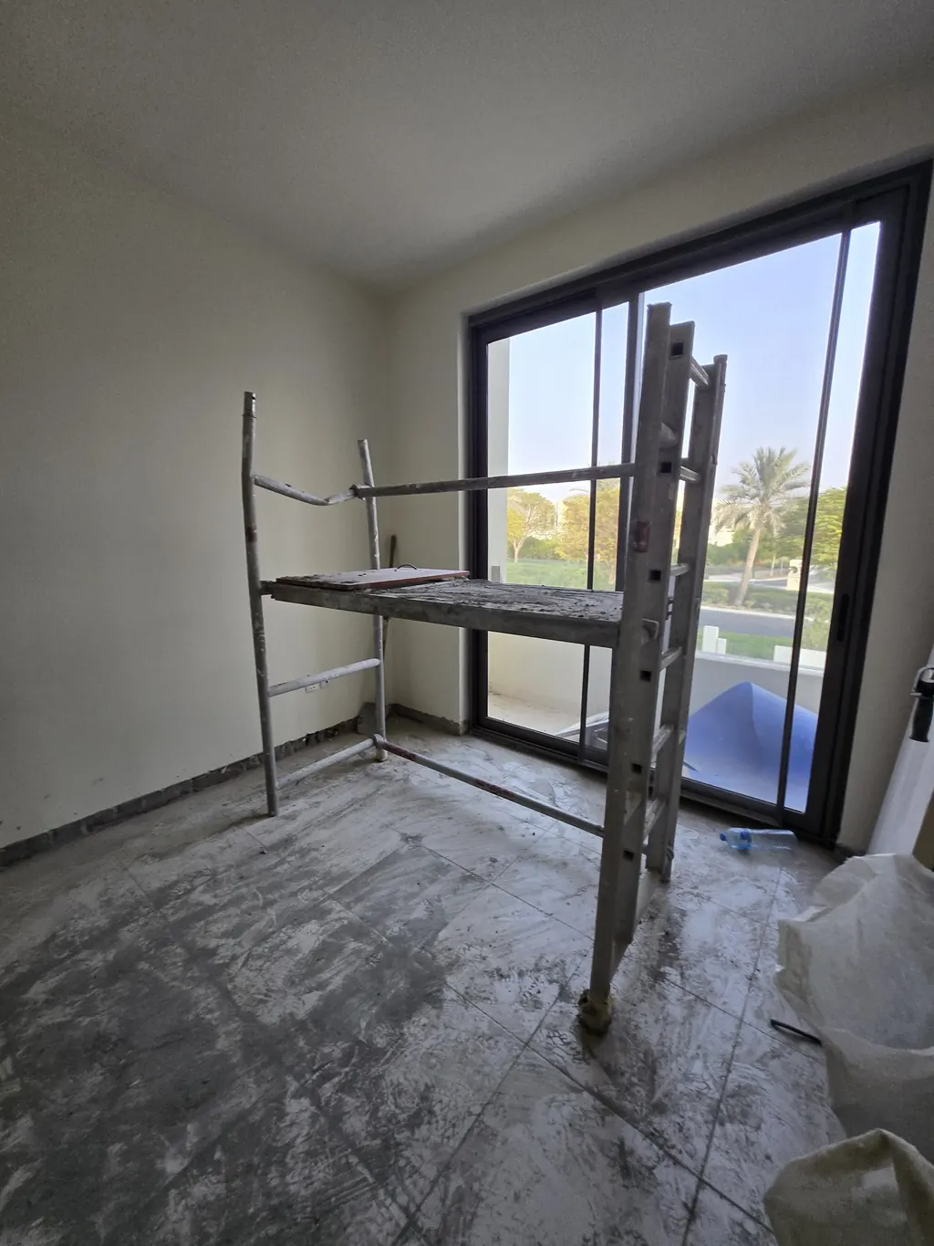 Living room of a Mira Oasis townhouse at strip-out: old finishes removed, scaffold up, outside doors beyond