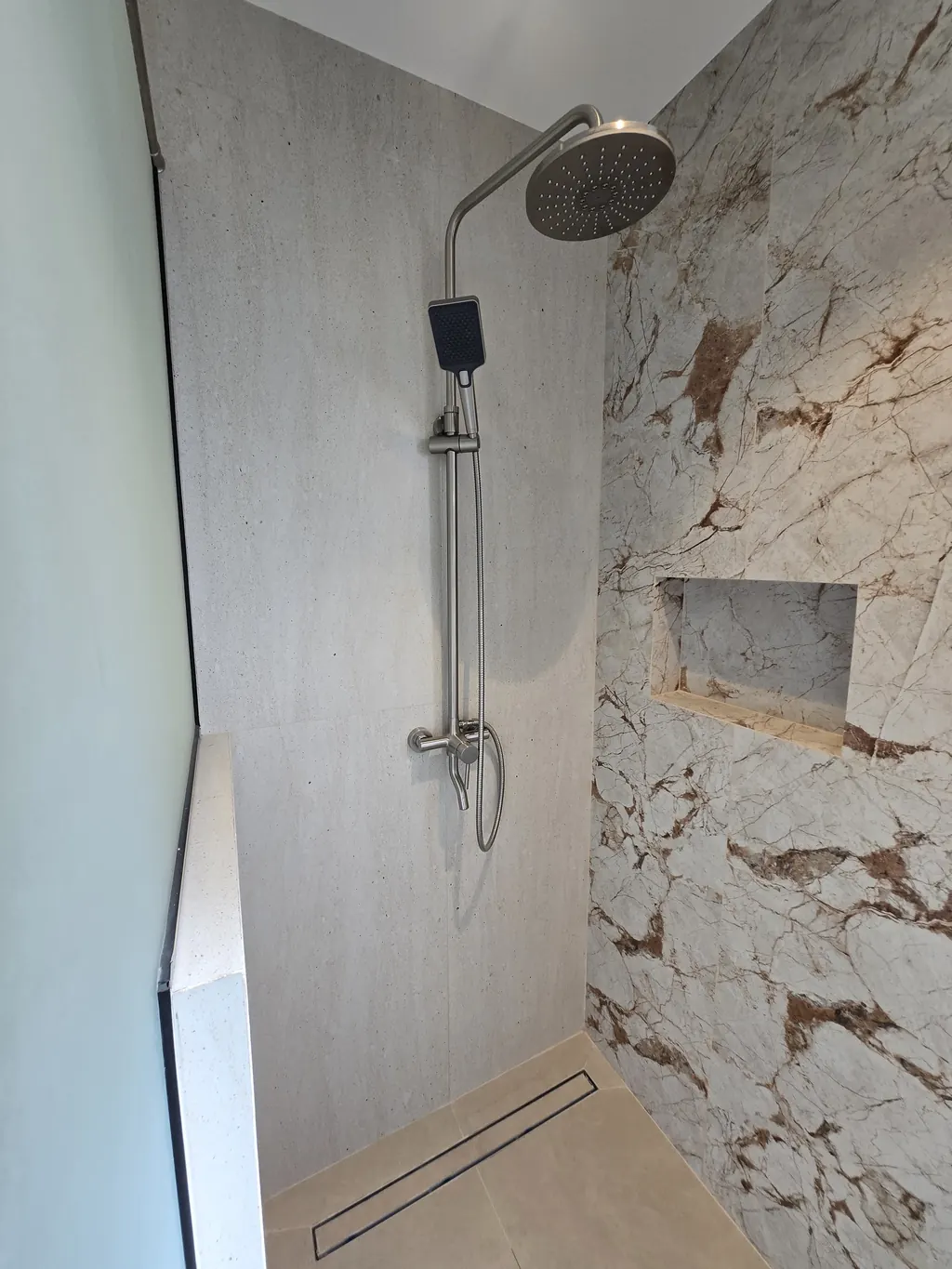 Shower in book-matched stone-look tile with a niche and linear drain